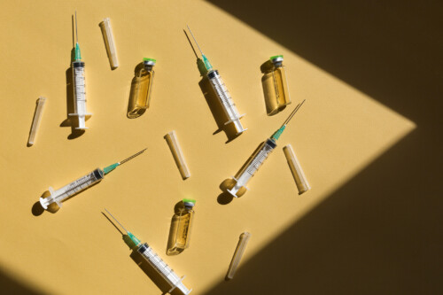 Syringe and Vaccine against yellow background top view